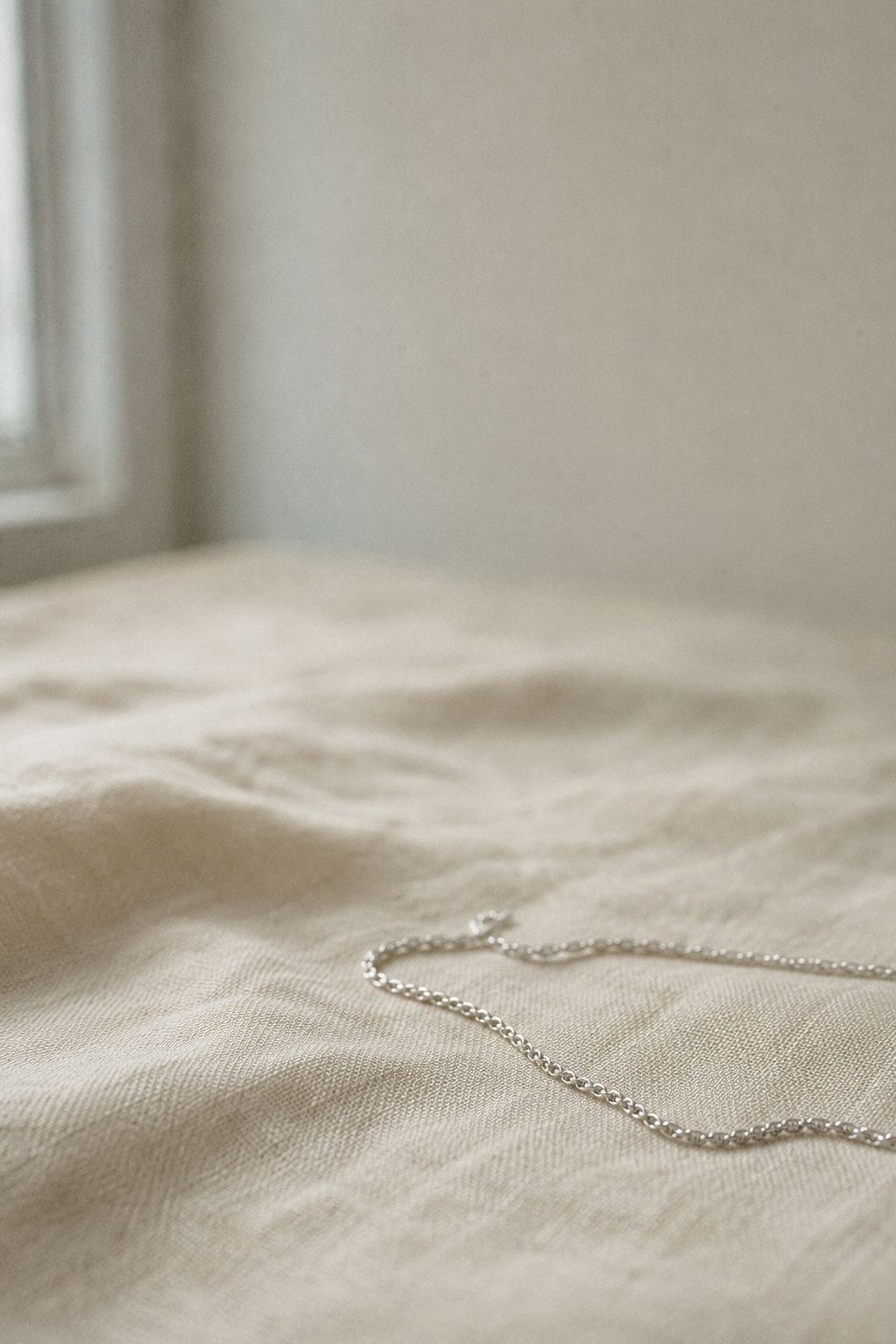 Fine white gold mangalsutra chain resting on cream linen in soft, cool natural light